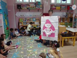 Bambini in cerchio che ascoltano la maestra, la quale mostra un cartellone con un mago disegnato che dice abracadabra